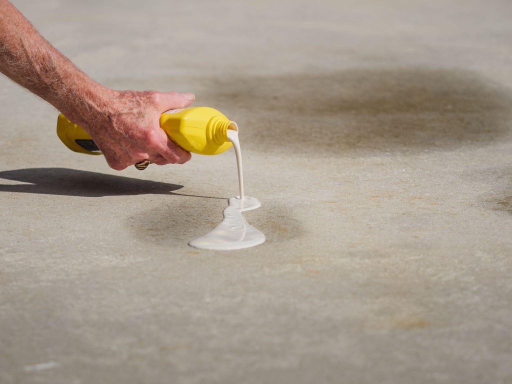 Man applying oil stain remover to concrete driveway