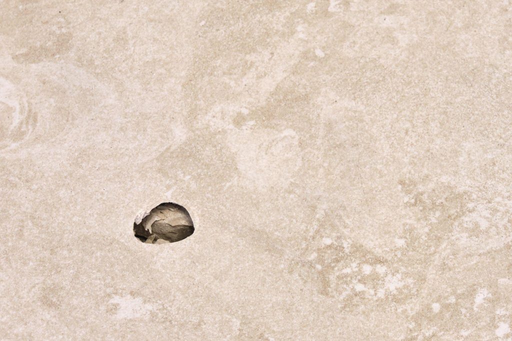 A hole in a beige floor tile, close up of damage
